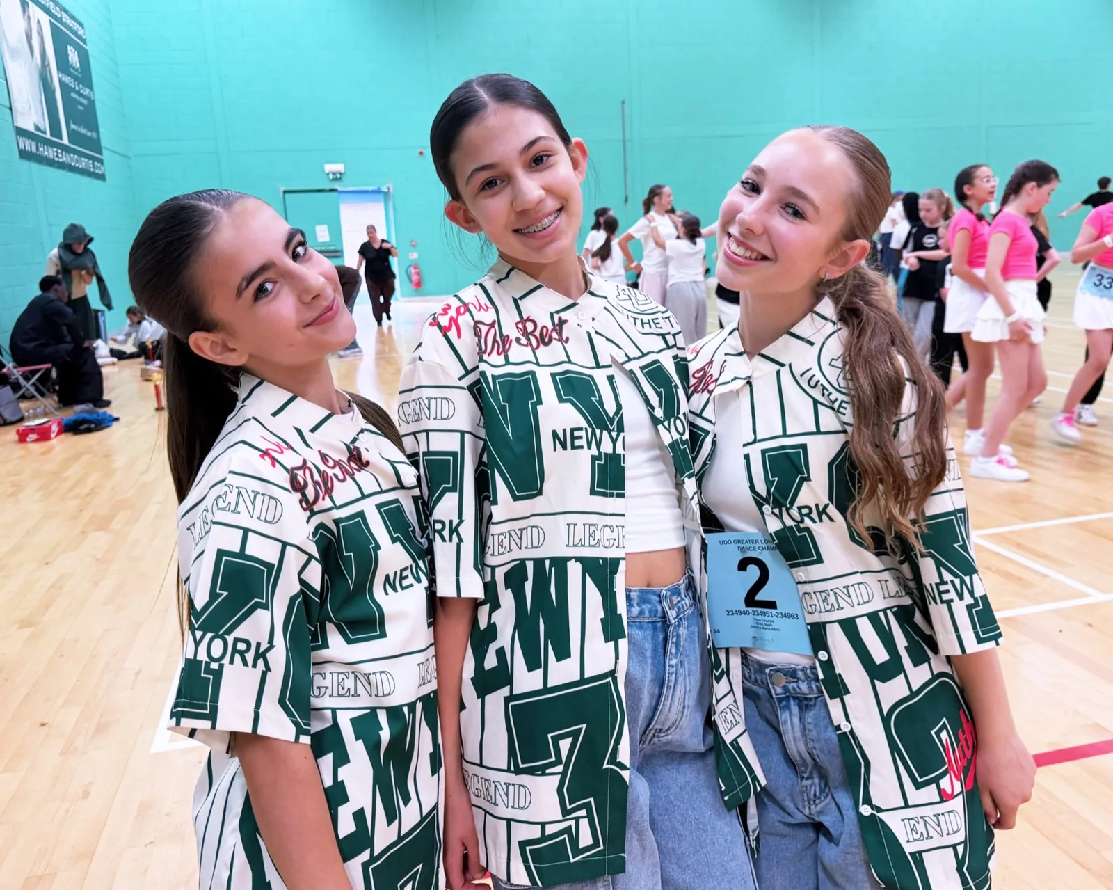 Three HK Teens dancers in matching New York print shirts at a UDO competition, smiling for the camera.