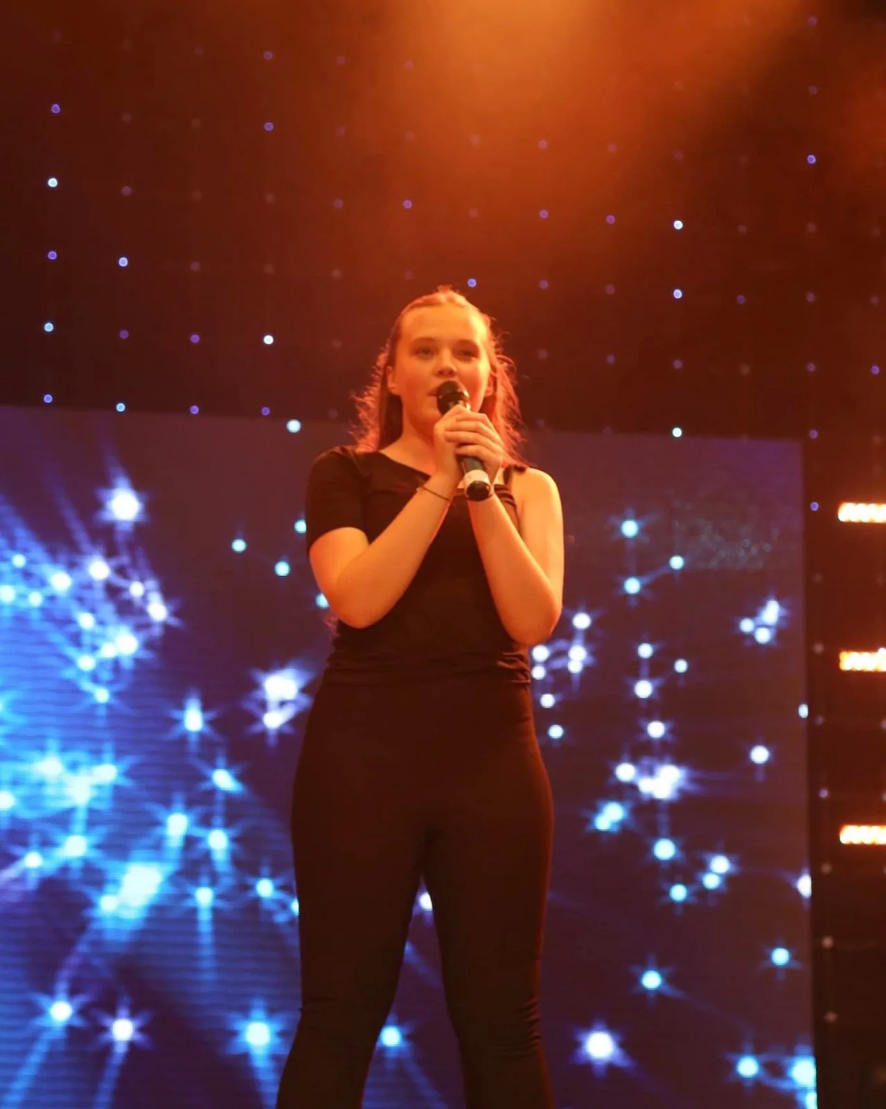 HK Dance Studios student singing solo on stage under lights, against a starlit backdrop.